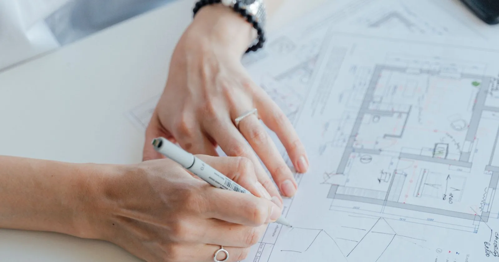 Mains annotant au stylo un plan de bâtiment posé sur un bureau
